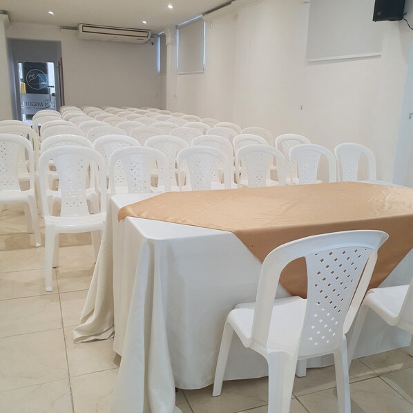 A conference room with a round table covered with a beige tablecloth, surrounded by white plastic chairs. - Hotel San Miguel Imperial (Santa Marta)