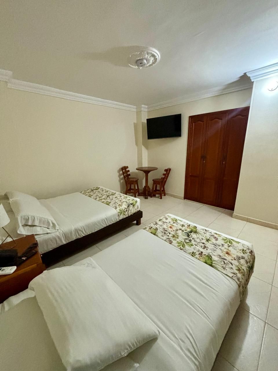 Una habitación con dos camas, un televisor montado en la pared, una mesita con sillas y un armario de madera.