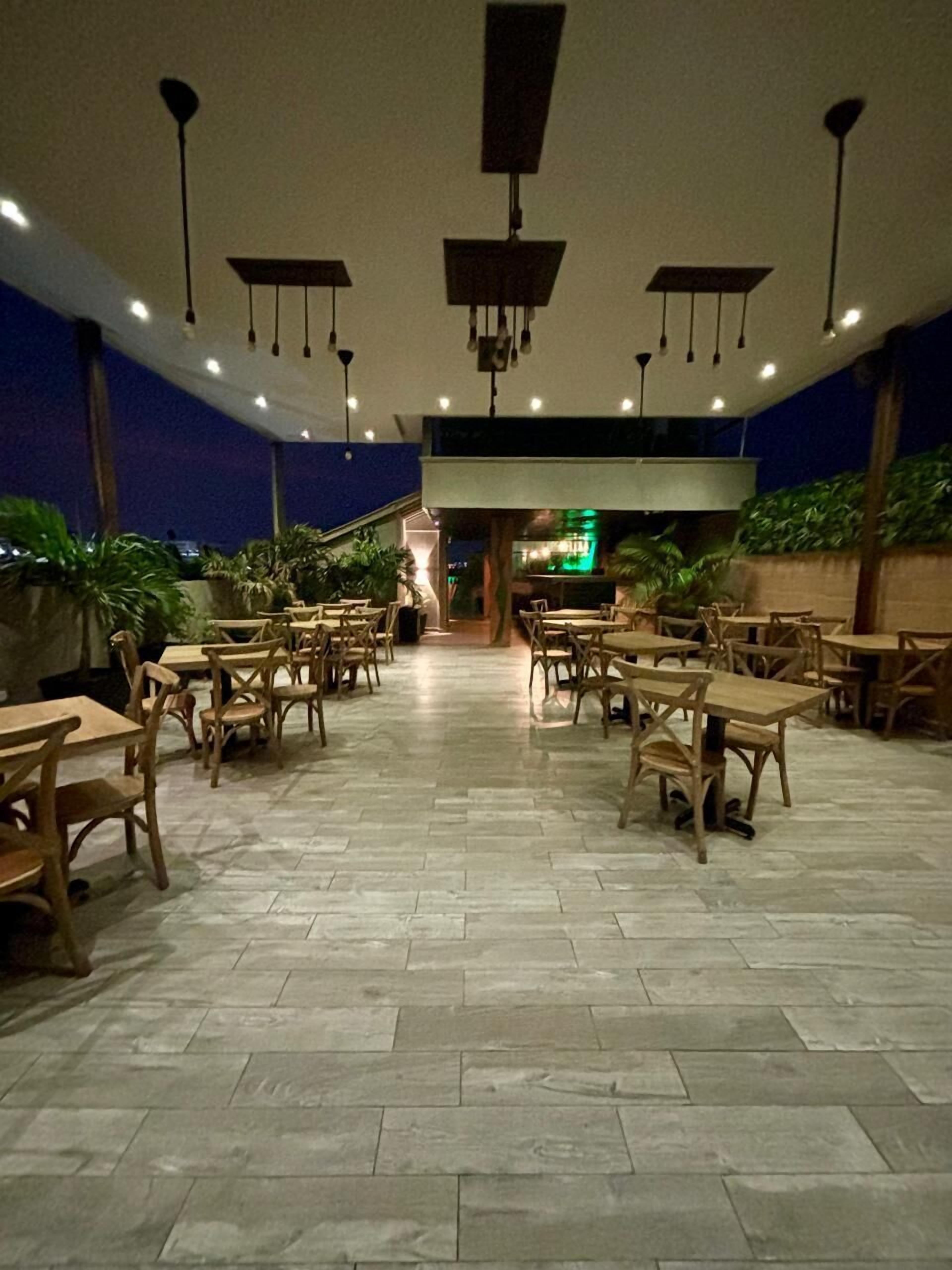 An indoor dining area with wooden tables and chairs, a tiled floor, and hanging pendant lights.