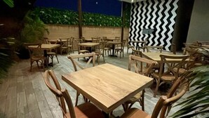 Zona pranzo all'aperto con tavoli e sedie in legno, parete decorata e lampade a sospensione.