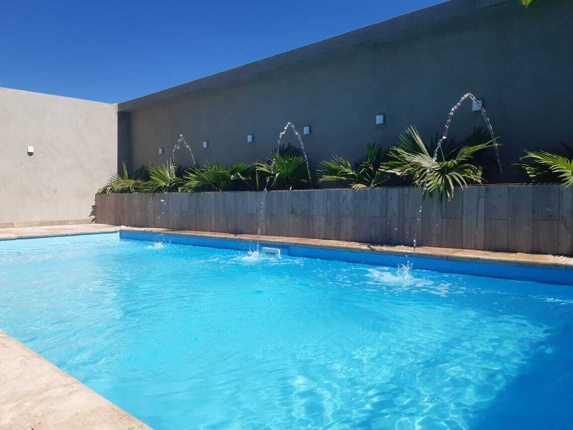 A swimming pool with clear blue water, surrounded by a low stone wall and lush green plants.