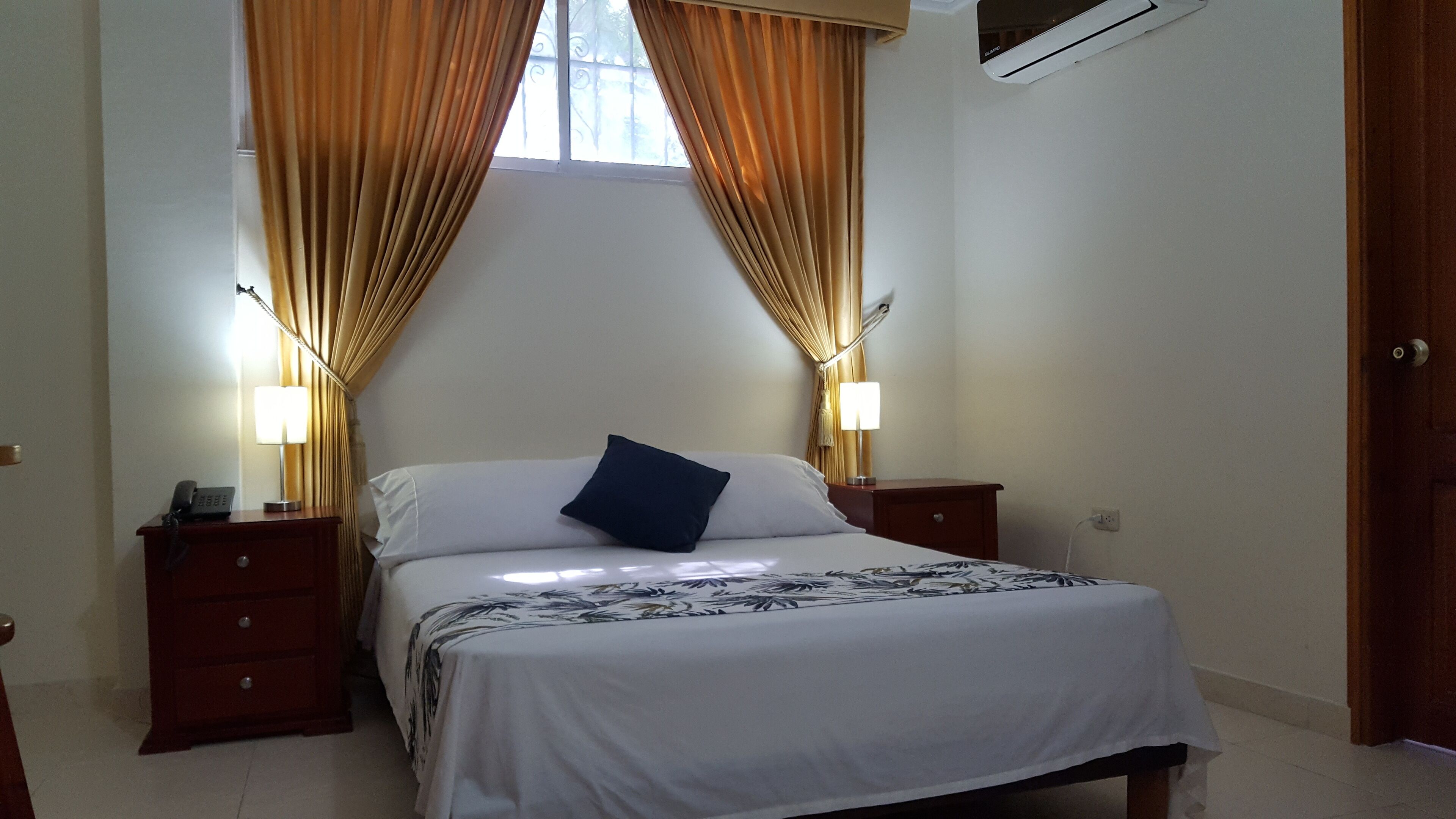 Una camera d'albergo con un letto, due comodini, un tavolo di notte, una lampada e tende.