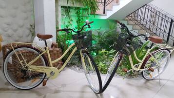Dues bicicletes amb cistelles de vimet, una cadira de vimet i una paret vegetal verda al fons.