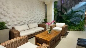 Un soggiorno moderno con mobili in vimini, una parete bianca strutturata, una ventola a soffitto e una scala che conduce a un piano superiore.