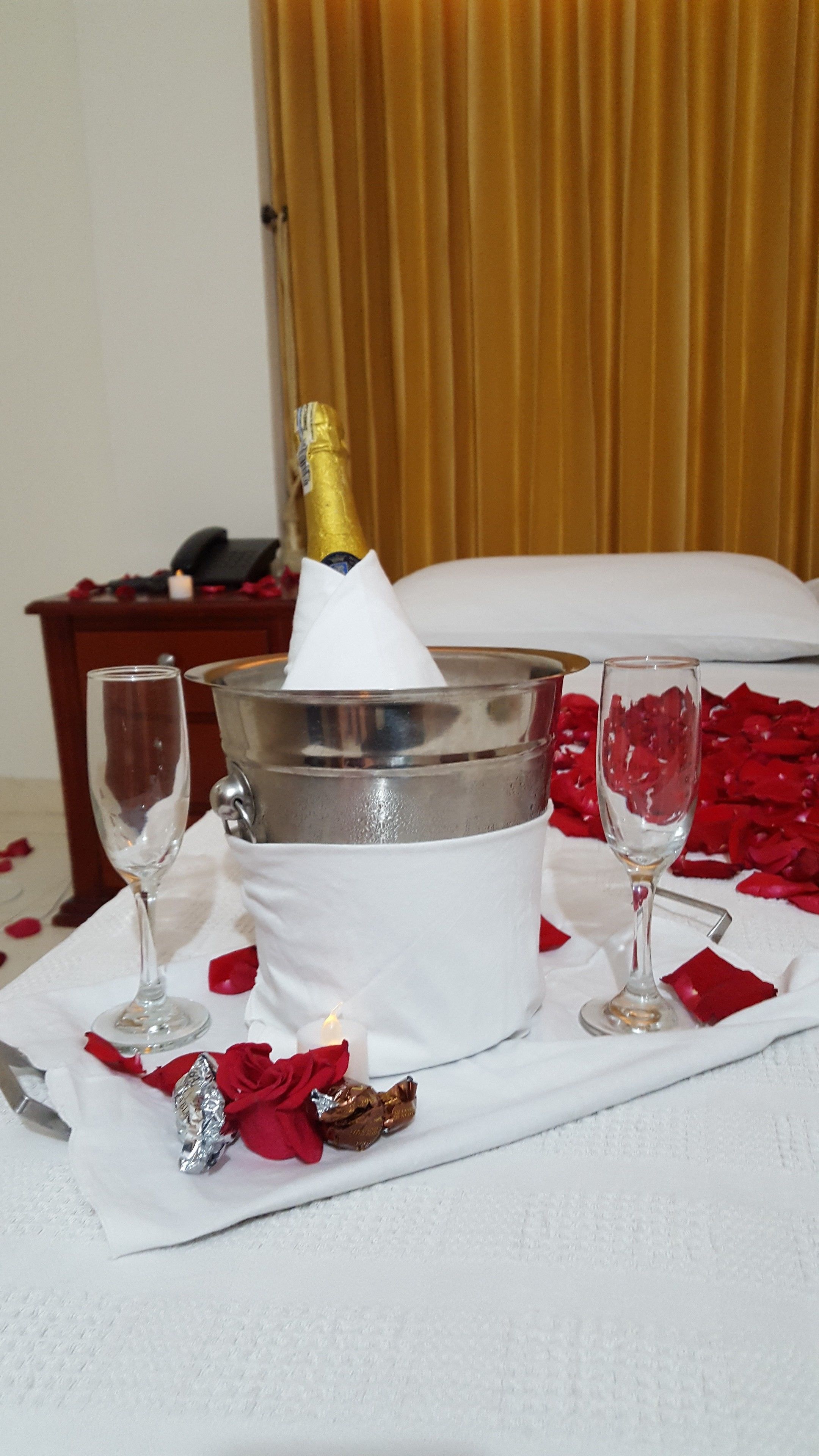 A table with a champagne bucket, two glasses, and rose petals.