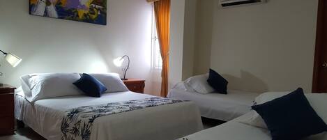 A hotel room with two beds, a painting on the wall, an air conditioner, and a window with curtains.