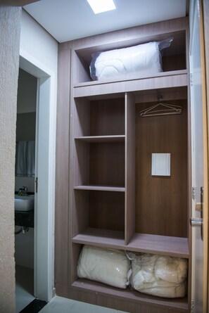 A walk-in closet with multiple shelves, a hanging rod, and a door with a light switch. - Iguassu Express Hotel (Foz do Iguaçu)