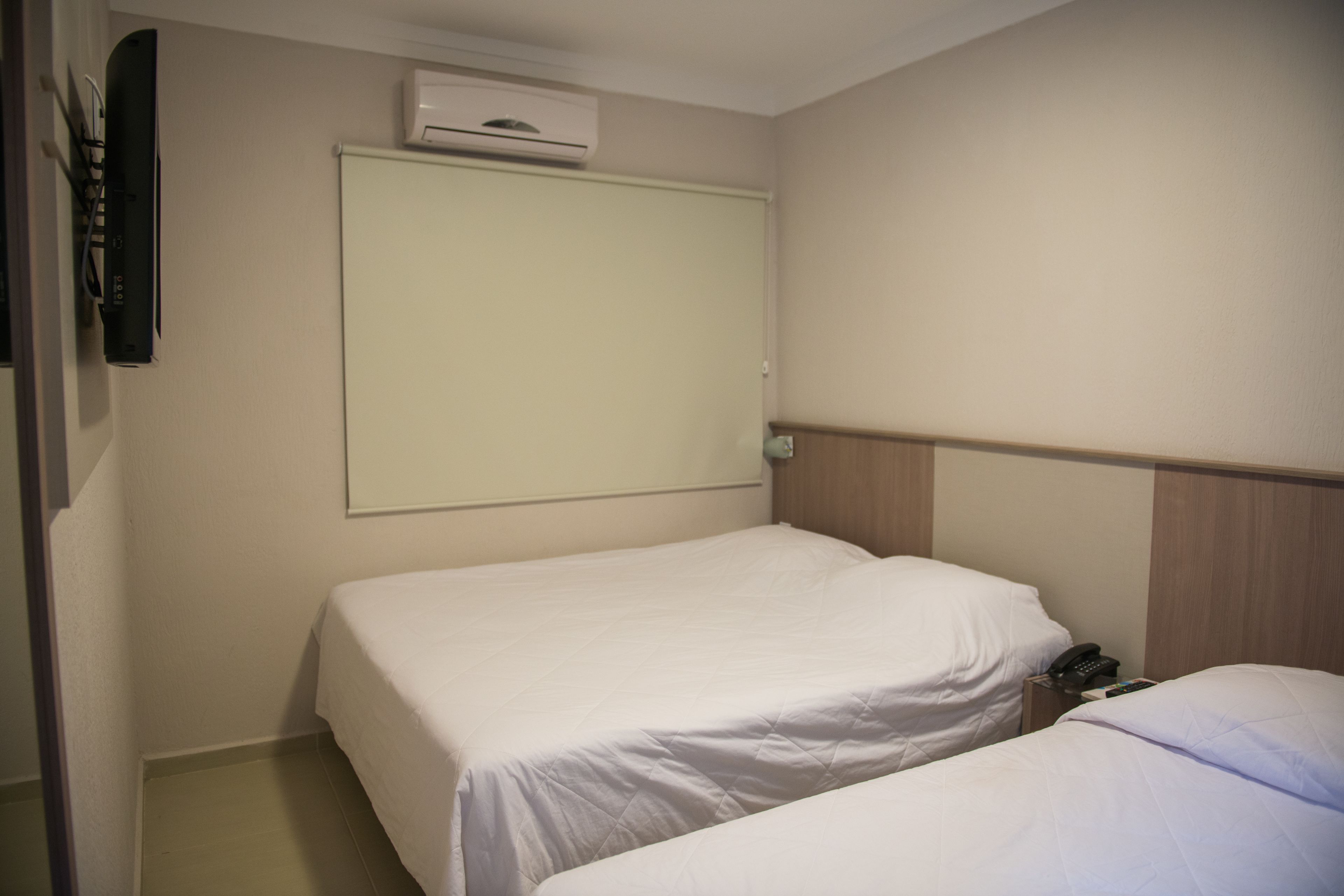 Habitación de hotel con dos camas individuales, aire acondicionado en la pared y teléfono en la mesita de noche.