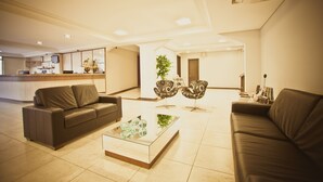 A modern living room with a sofa, a coffee table, and two patterned chairs. A kitchen area is visible in the background. - Iguassu Express Hotel (Foz do Iguaçu)