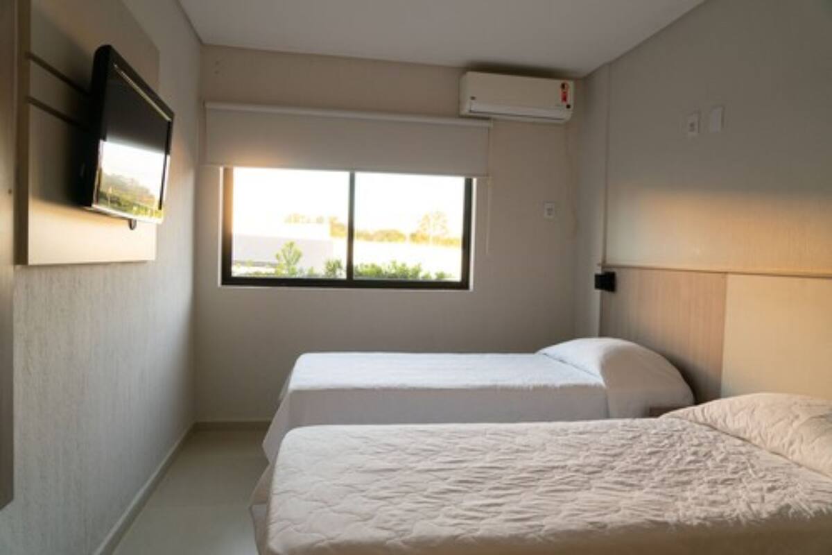 A hotel room with two beds, a TV mounted on the wall, and a window providing a view of the outdoors.