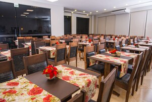 Un restaurante con varias mesas y sillas, cada una con mantel floral y un pequeño jarrón con arreglo de flores rojas.