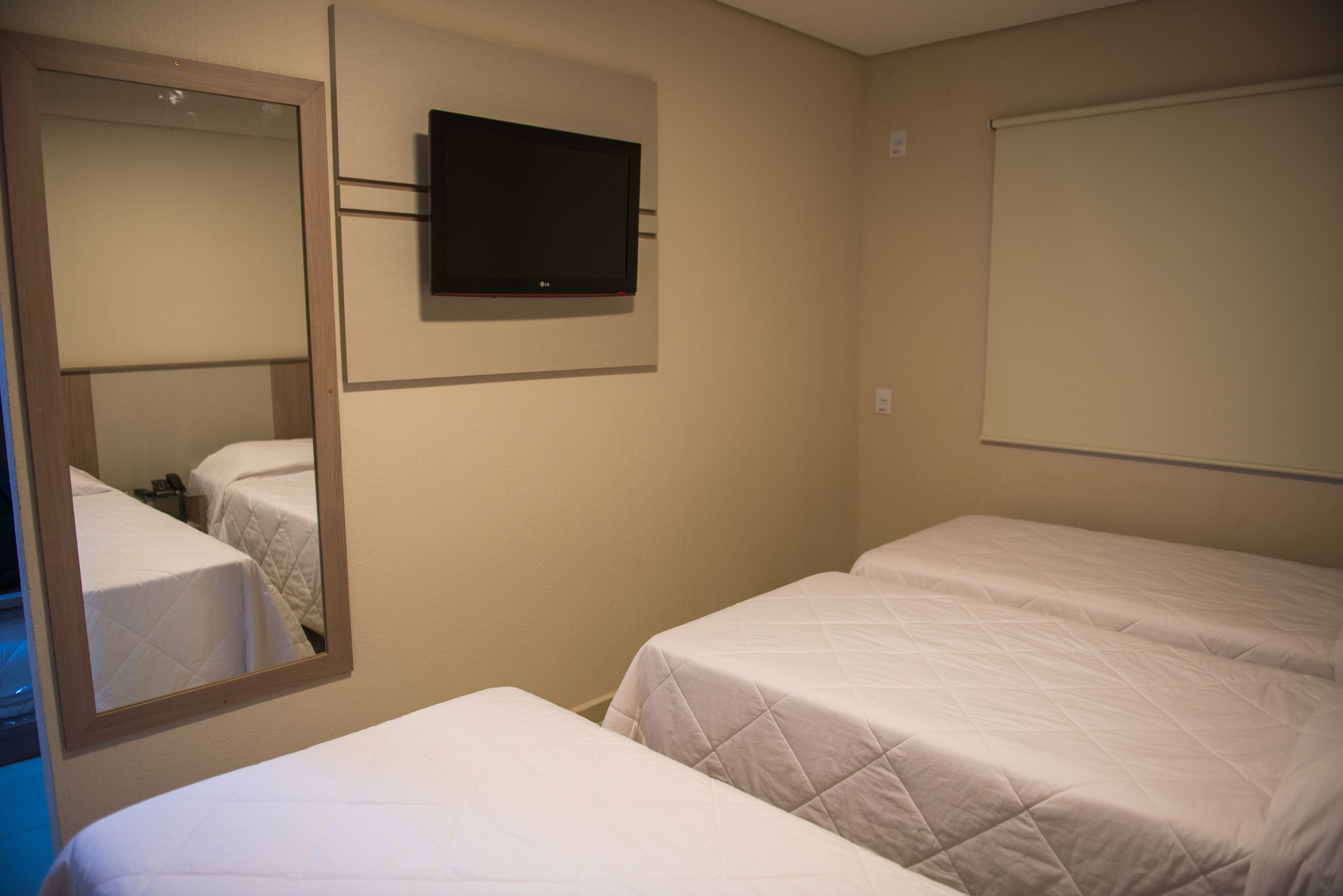 A hotel room with two single beds, a flat-screen TV mounted on the wall, and a large mirror reflecting the room.