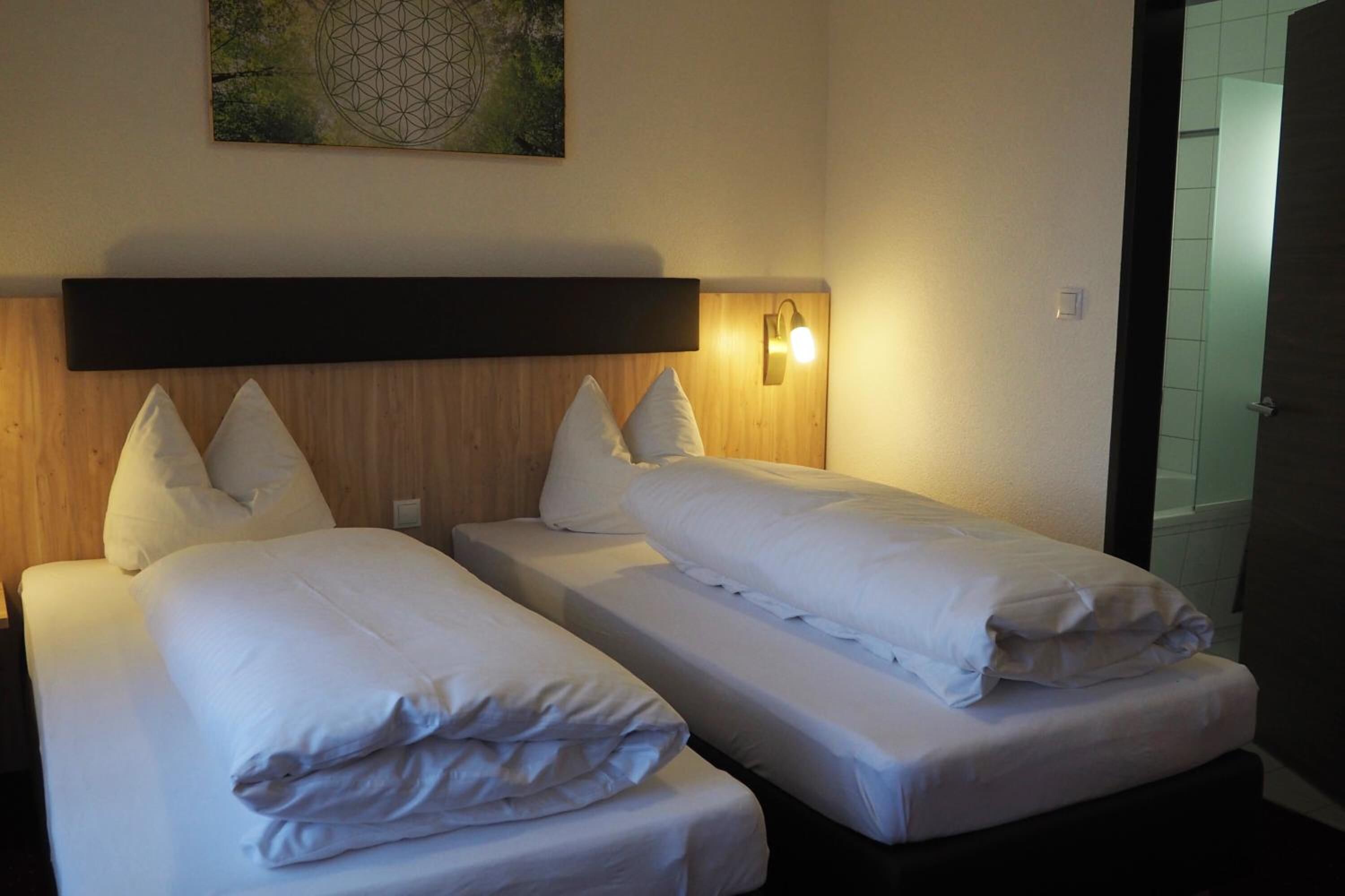 Habitación de hotel con dos camas individuales, cabecero de madera, luz de pared y un cuadro sobre la cama.