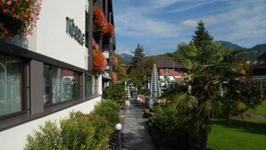 A hotel with a pathway leading to the entrance, surrounded by greenery and a mountain backdrop. - Hotel Rössle (Roethis)