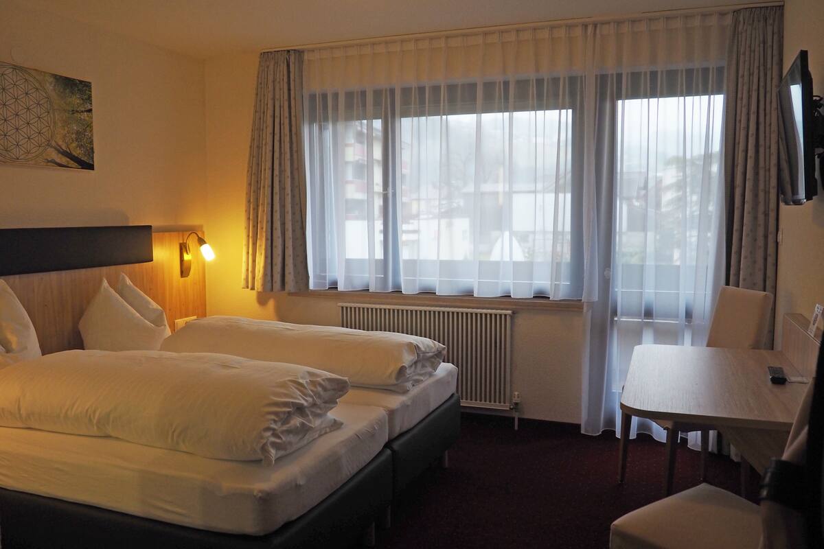 Habitación de hotel con dos camas, un escritorio, una silla, un televisor y una ventana con cortinas.
