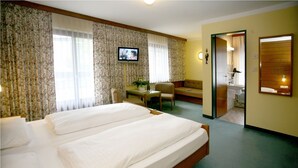 A hotel room with a large bed, a television, a desk with a chair, and a bathroom visible through an open door. - Hotel Rössle (Roethis)