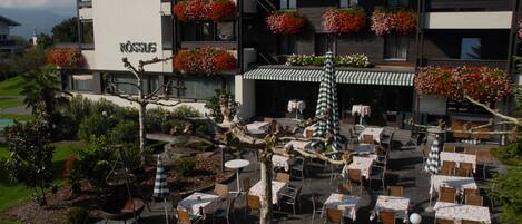 Un hotel con terraza exterior, jardineras en los balcones y un jardín cuidado.