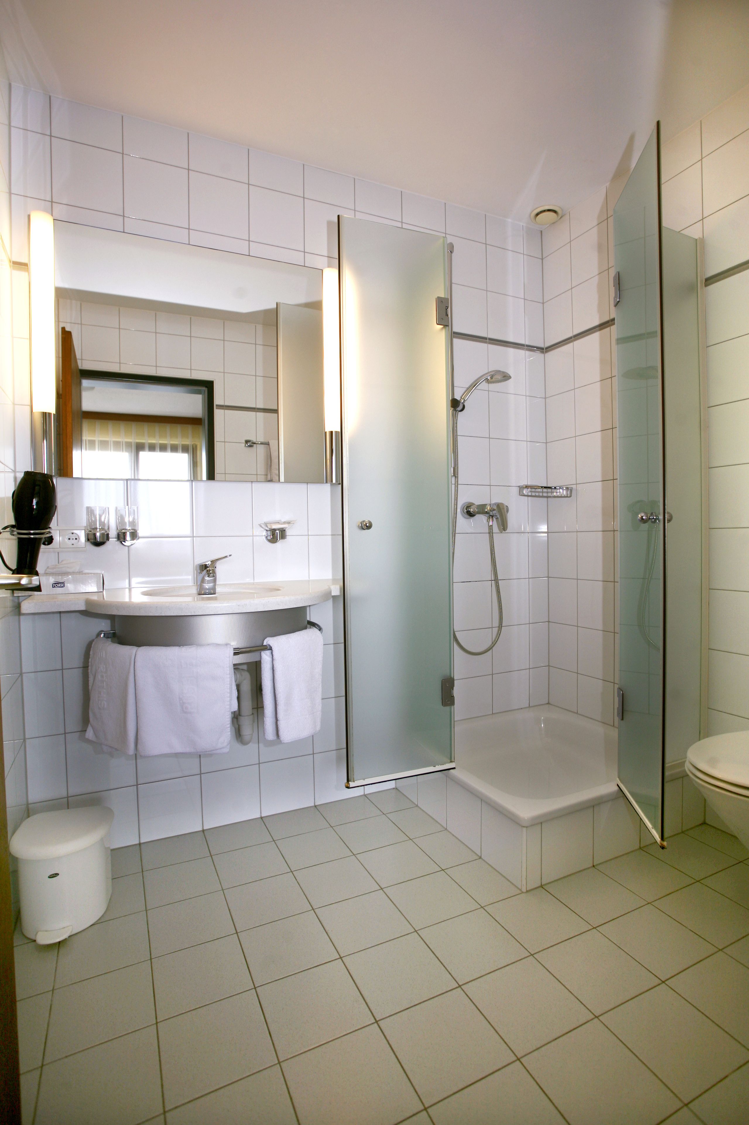 Et moderne badeværelse med en glasafskærmet brusekabine, en hvid vask og et toilet.