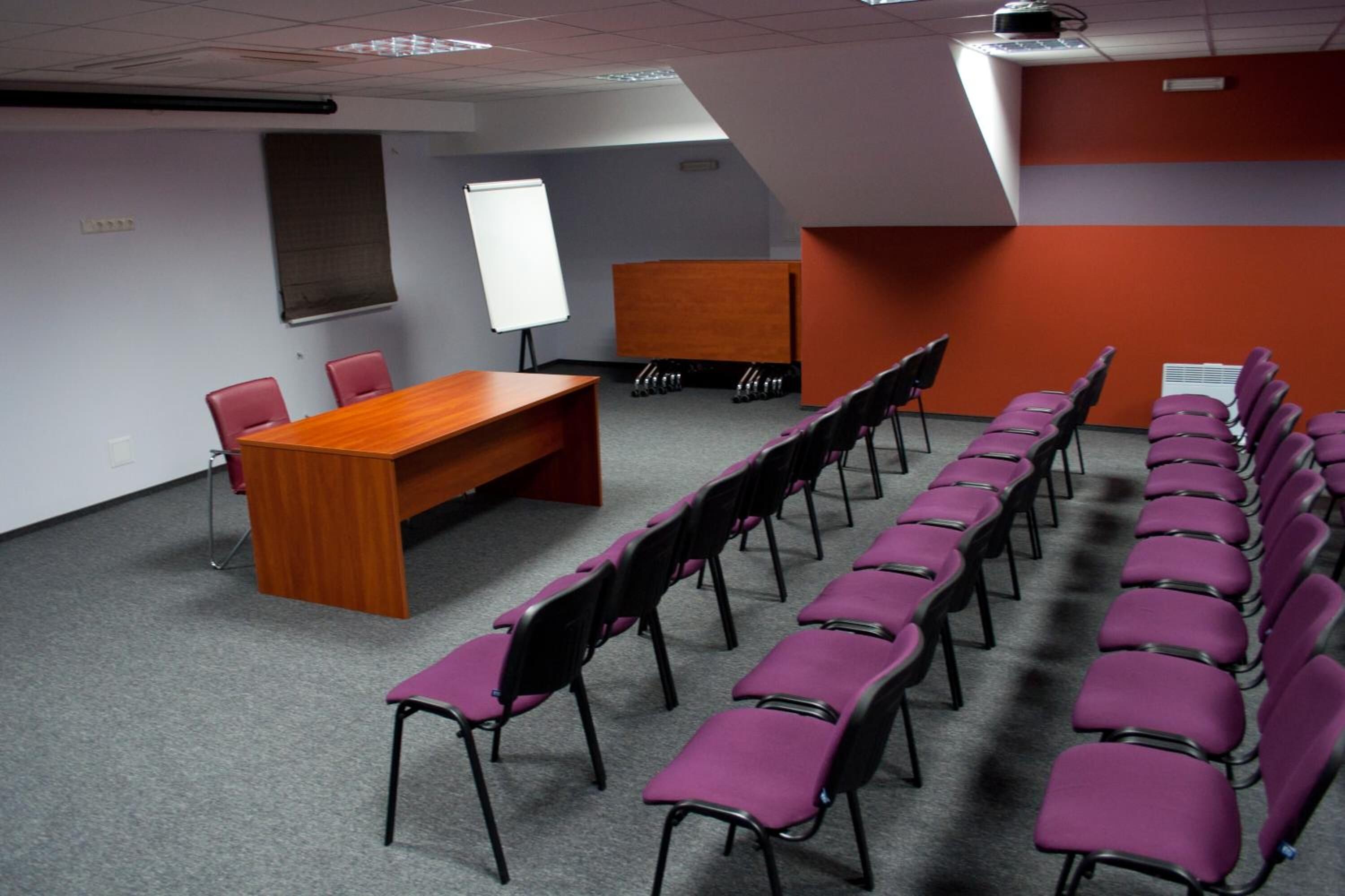 Una sala de conferencias con una larga mesa, filas de sillas, una pizarra y un proyector.