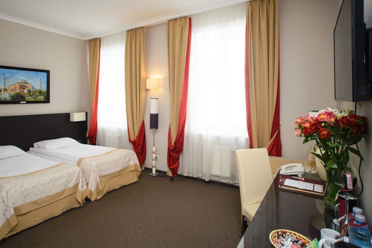 A hotel room with two beds, a desk with a chair, a TV, a lamp, and a vase of flowers.
