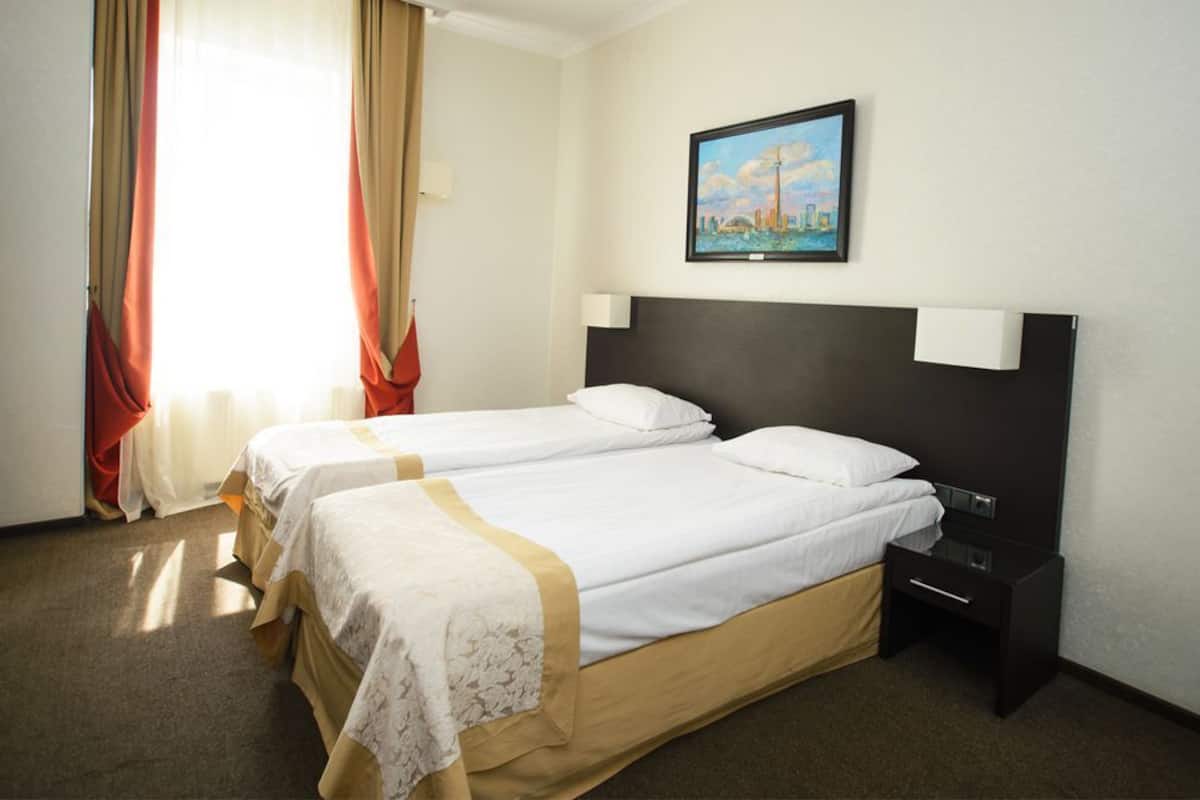 A hotel room with two beds, a nightstand, a lamp, and a painting on the wall.