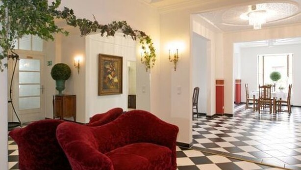 Una habitación con piso a cuadros, un sofá rojo, un cuadro en la pared y un candelabro.