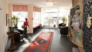 Un hall de hotel con alfombra estampada, una estatua y un amplio ventanal.