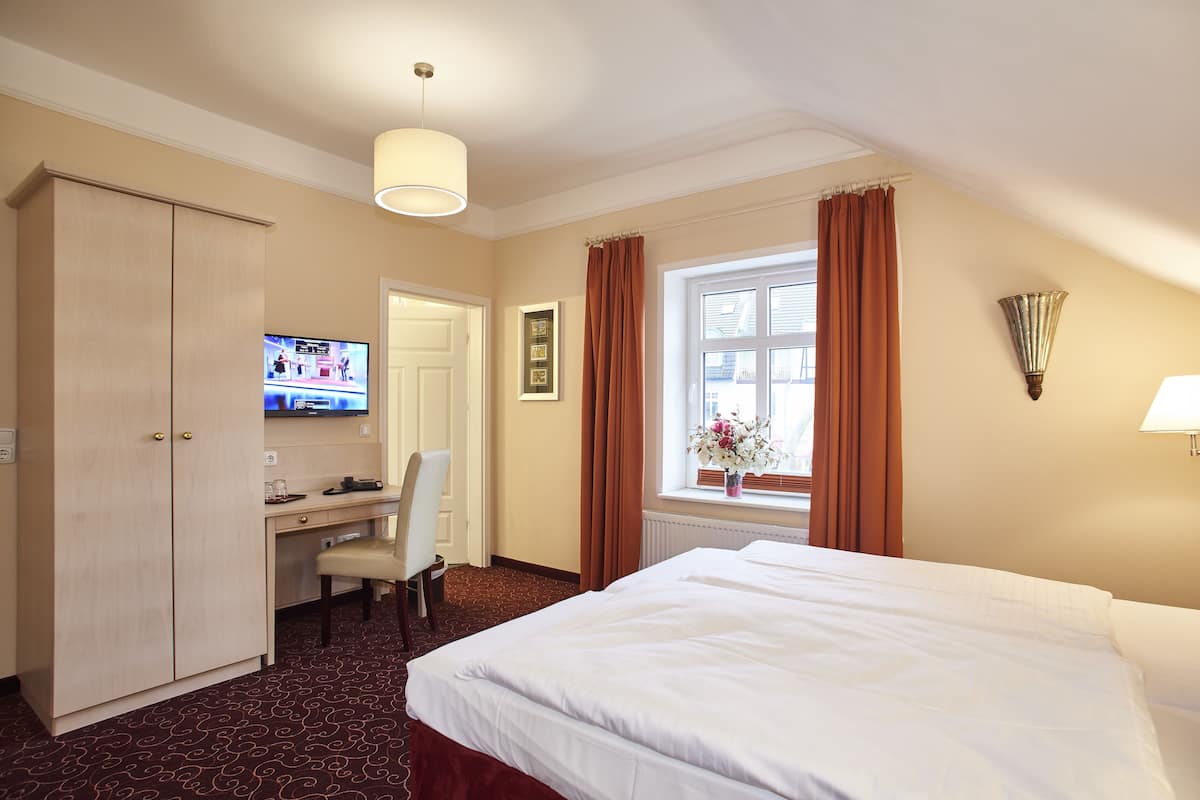 A hotel room with a bed, desk, chair, television, and curtains.