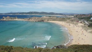 Una playa con aguas turquesas cristalinas, una orilla arenosa y una cadena montañosa distante.