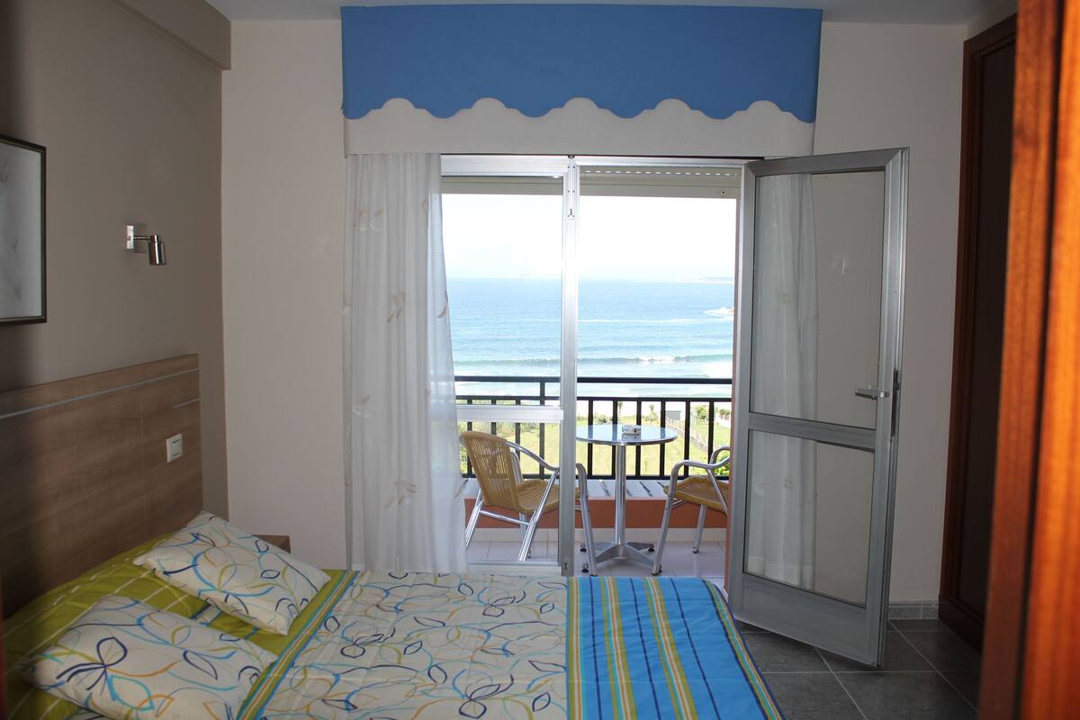 A bedroom with a bed, a balcony with a view of the ocean, and a door leading to the balcony.
