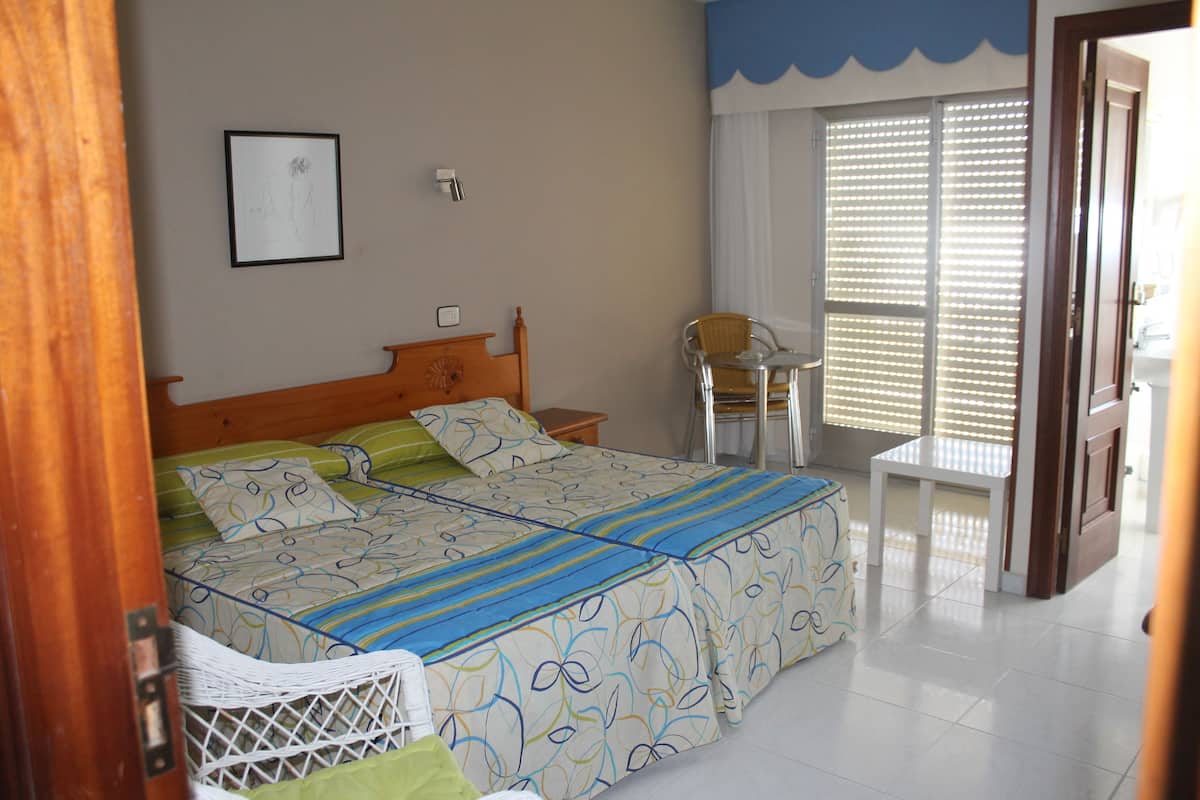 A bedroom with a bed, bedside table, chair, and a window with blinds.