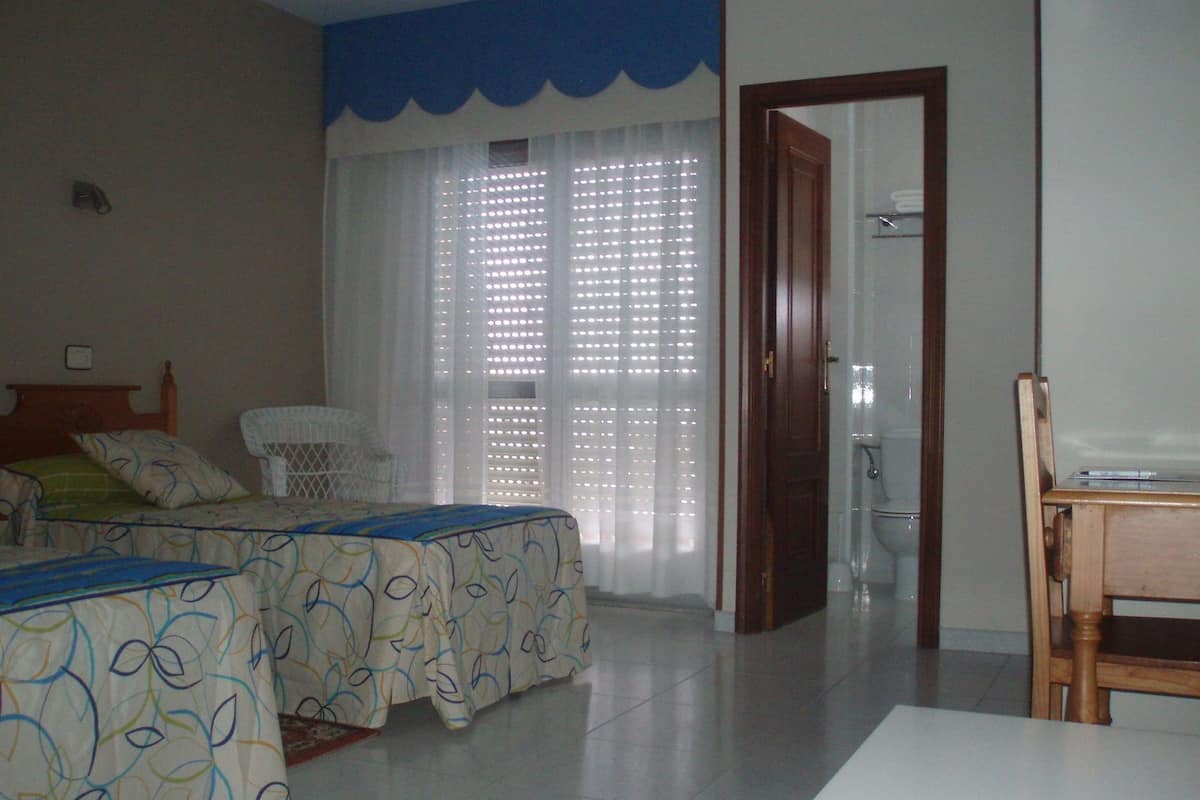 A bedroom with two beds, a chair, a table, and a bathroom visible through a door.