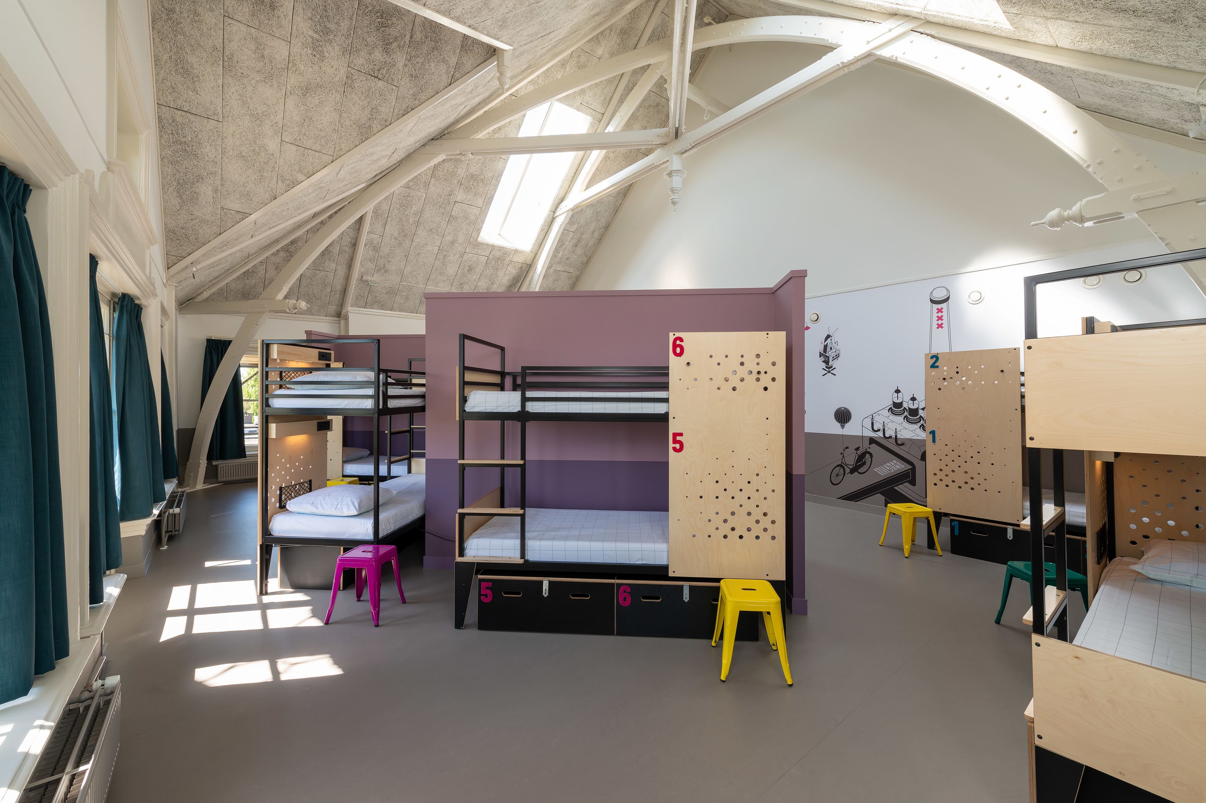 A dormitory room with bunk beds, numbered storage compartments, and a mural on the wall.