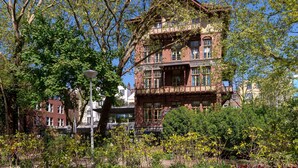 Een historisch gebouw met een balkon en meerdere ramen, omgeven door weelderige begroeiing.