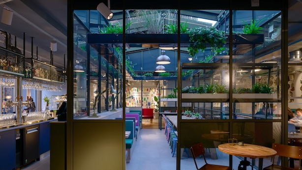 Een modern interieur met een bar, zitplaatsen en een glazen dak met planten.