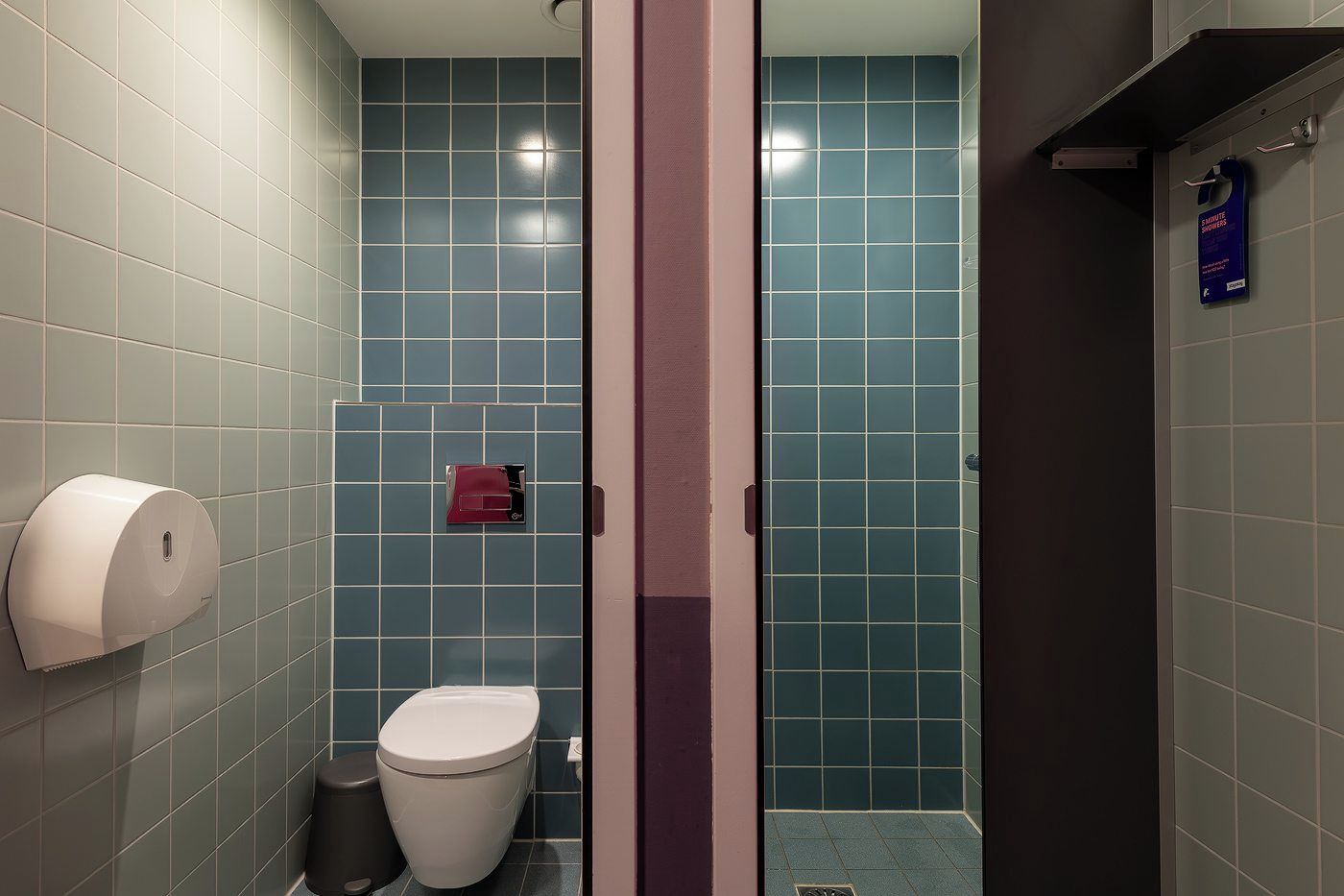 Un baño con inodoro, dispensador de toallas de papel y zona de ducha.