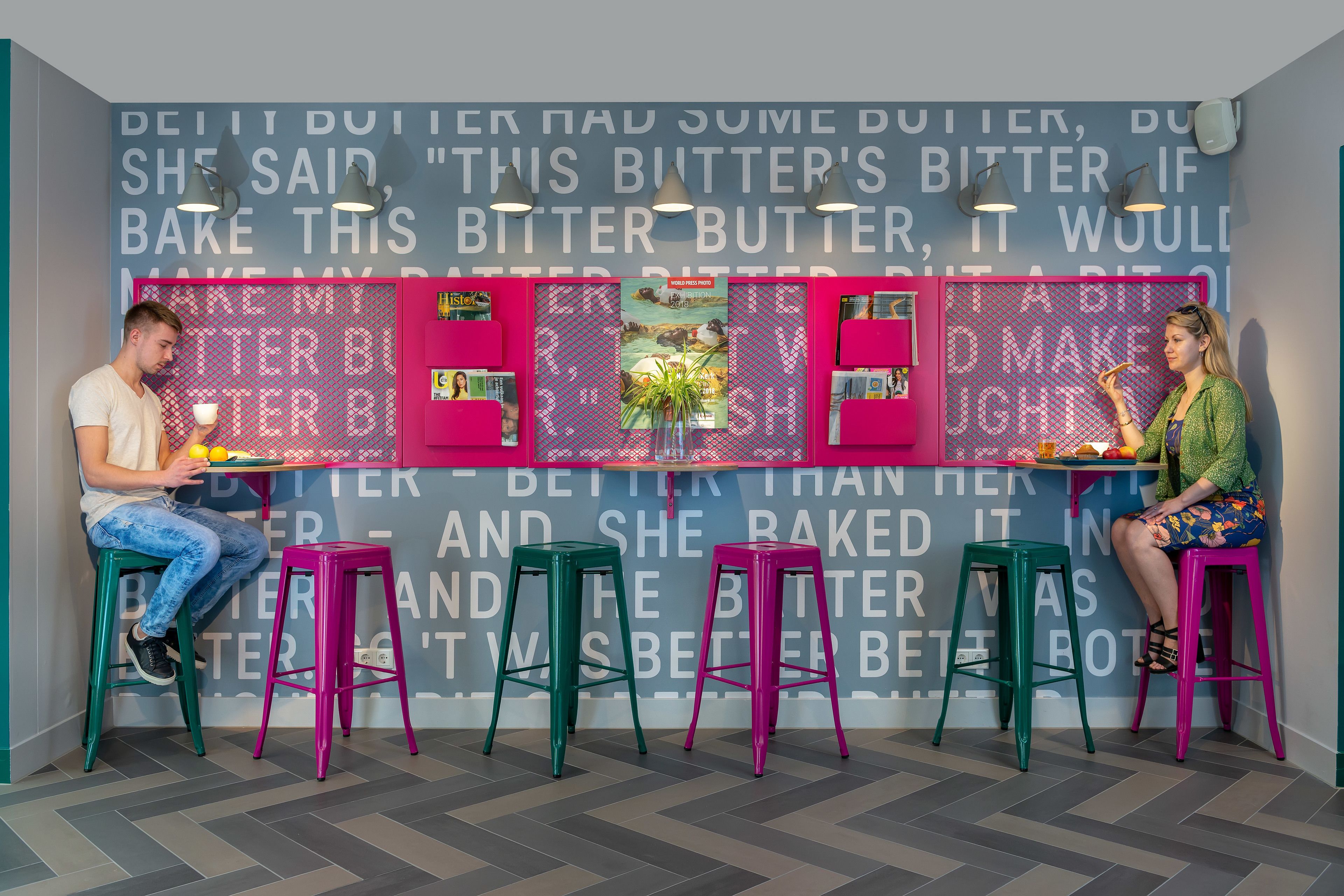 A kitchen area with a counter, two stools, and a wall with a repeated text pattern.