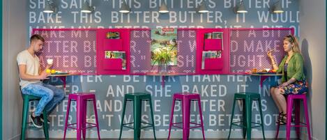 A kitchen area with a counter, two stools, and a wall with a repeated text pattern.