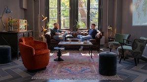 Een gezellige woonkamer met een leren bank, een bijzettafeltje en een groot raam met uitzicht op bomen.