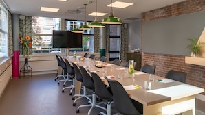 Een congrescentrum met een lange tafel, zwarte stoelen en groene hanglampen.