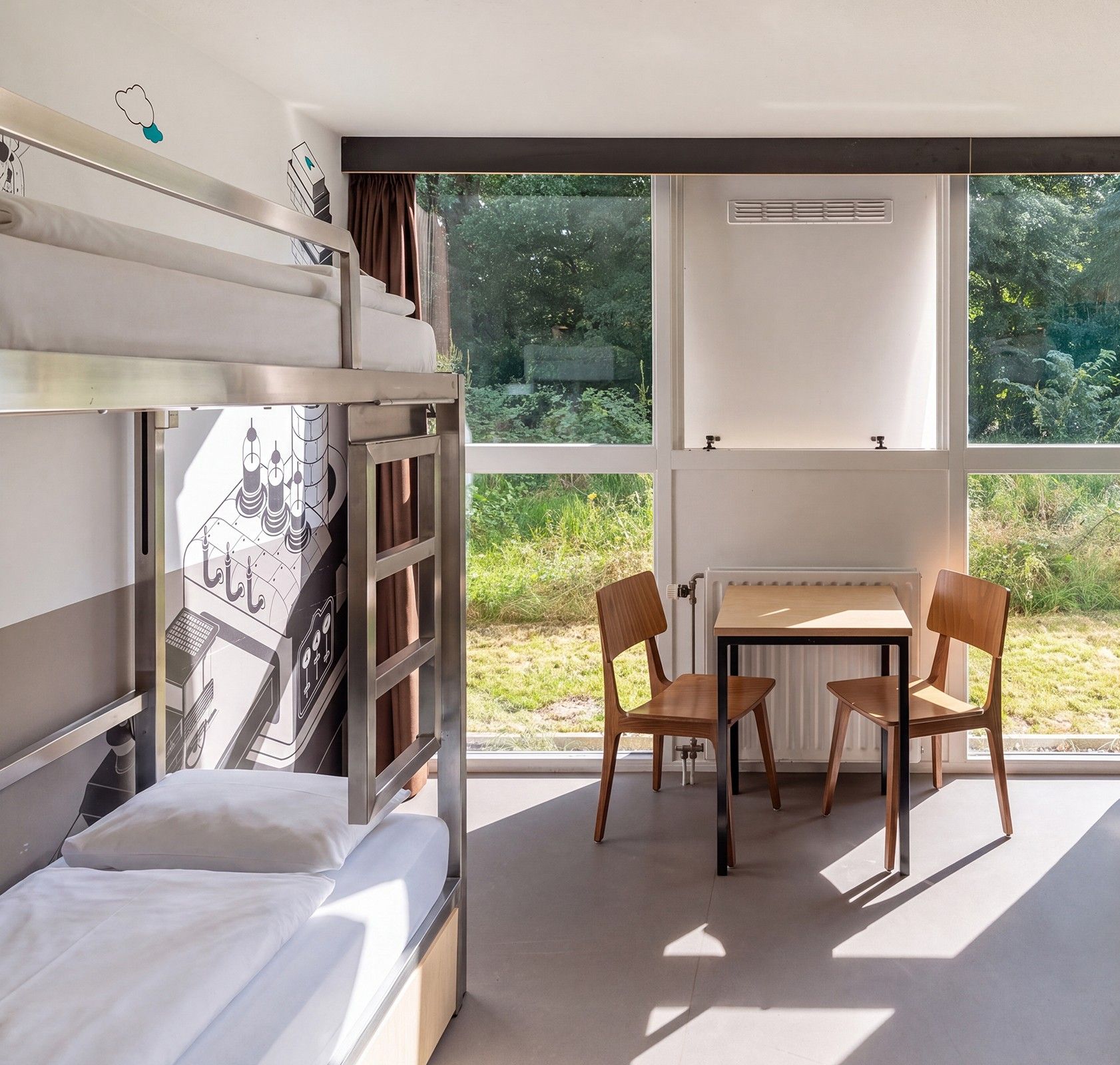 Una cama litera con ventana, una mesa y dos sillas en una habitación con vista a la vegetación.