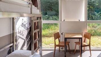Una cama litera con ventana, una mesa y dos sillas en una habitación con vista a la vegetación.