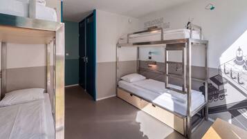 A bunk bed room with a bunk bed on the left and a single bed on the right, both with white bedding. There is a door leading to another room, and a wall with a welcome sign.