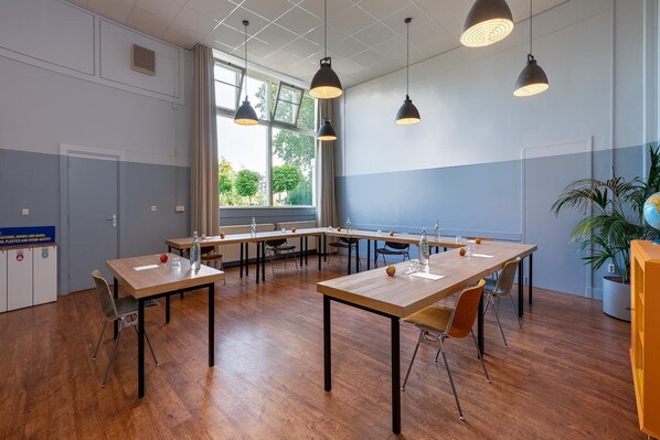 A conference room with multiple tables and chairs, large windows, and hanging pendant lights.
