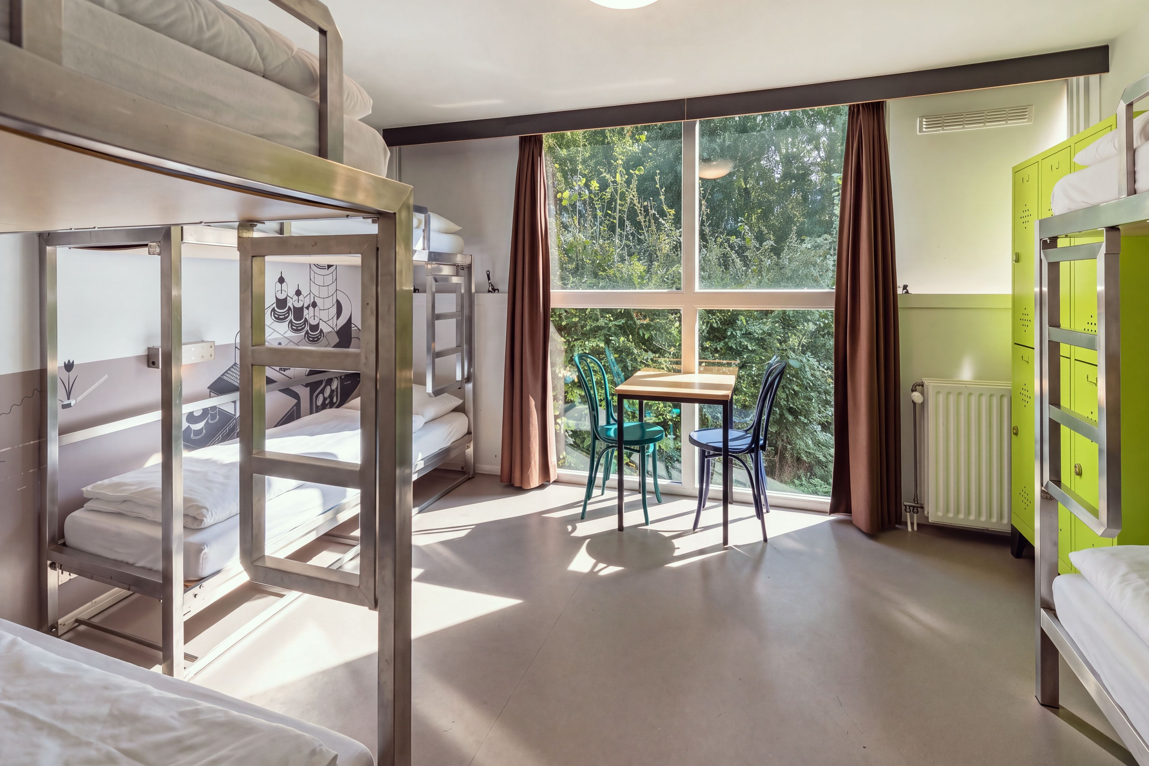 Un dormitorio con literas, una mesa con sillas, un radiador y una ventana con cortinas.