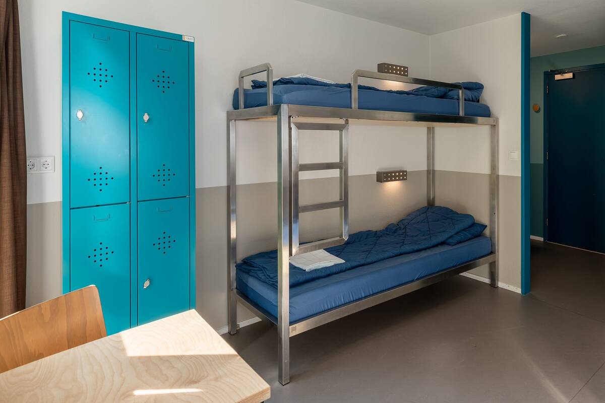 A bunk bed room with a desk and a blue wardrobe.
