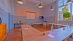 Un salón de conferencias con mesas y sillas de madera, una pantalla de proyector y una televisión.