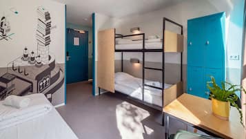 A hotel room with bunk beds, a desk, a chair, a plant, and a wall with a graphic design.