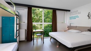 A hotel room with bunk beds, a desk, and a view of greenery outside. - Stayokay Haarlem - Hostel (Haarlem)
