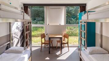 A bunk bed room with a desk and chairs, a radiator, and a view of greenery outside.